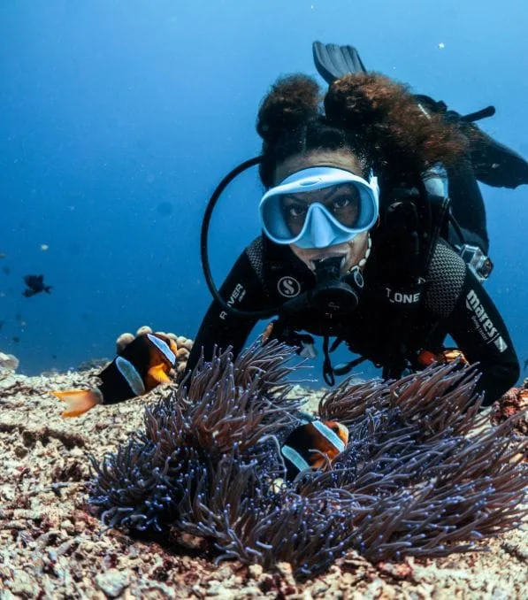 Adv Open Water Penida – 2 潜水员在努沙佩尼达(Nusa Penida)海底观察海葵和两条小丑鱼,戴着潜水面罩和呼吸器靠近海床。